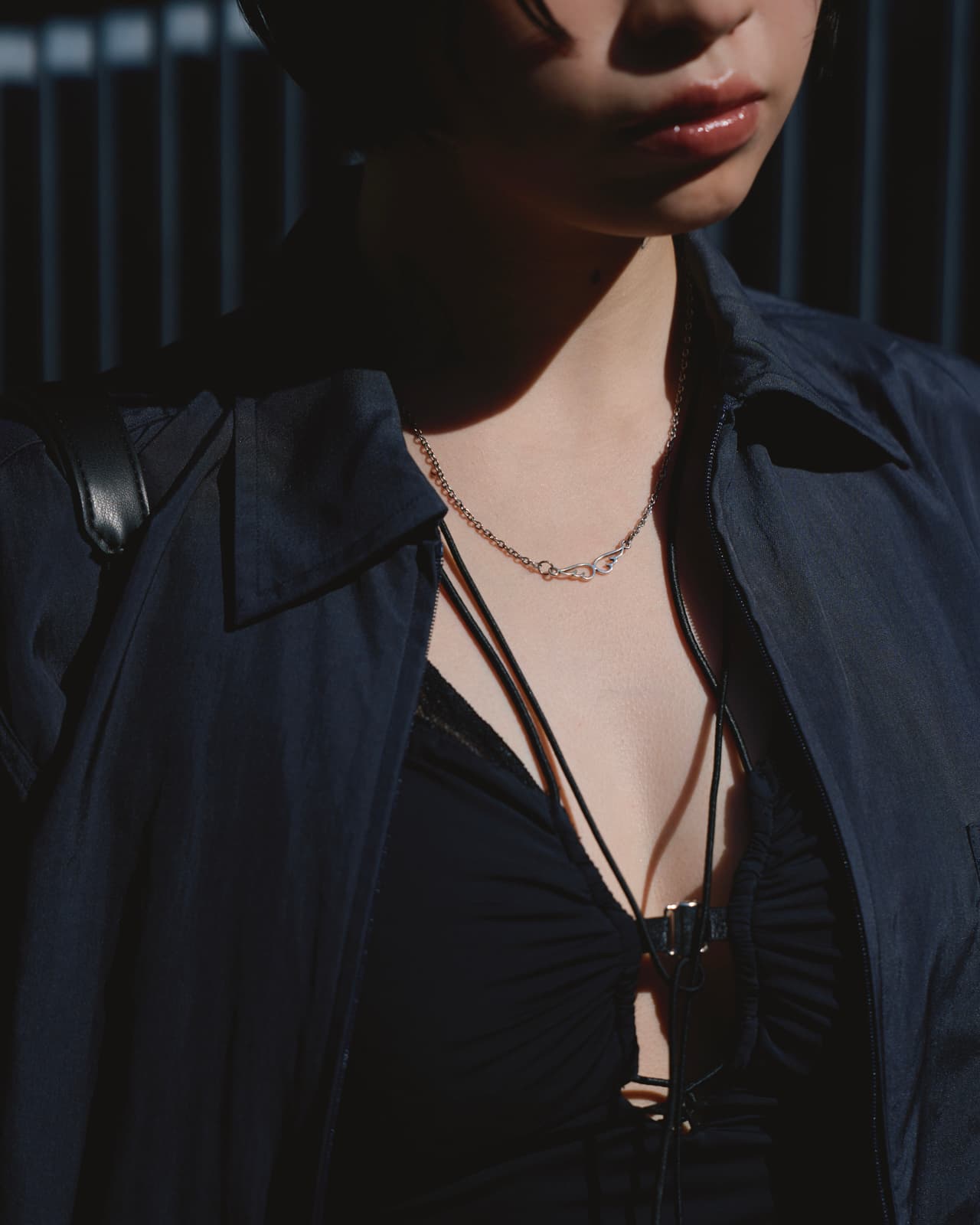 Close-up of a person wearing a dark jacket over a black top with a chain necklace and glossy lips.