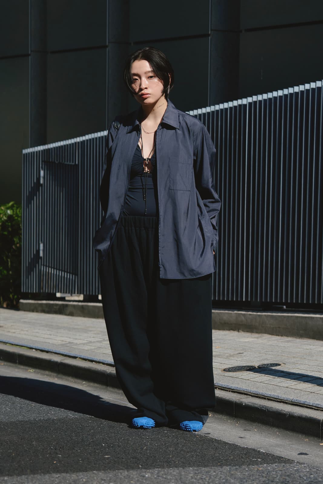 Person standing on a city street wearing a loose dark shirt, wide black pants, and bright blue tactile shoes.